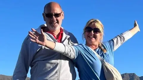 Facebook Andrew y Dawn Searle sonríen a la cámara mientras está parado afuera: está muy bien vestido con los brazos.