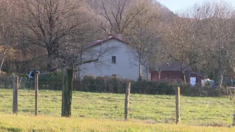 Francia Télévien en casa con paredes blancas, rodeada de árboles y piedras