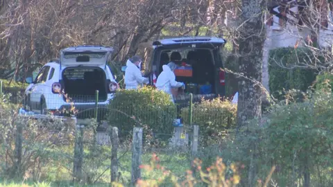 Los oficiales de Francia Téléviewer están tomando cajas o desde los zapatos de automóvil, y otro auto con su bota cerca de ellos. Los árboles y arbustos los giran.